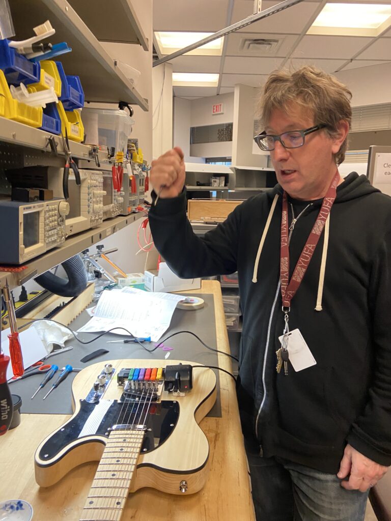 A photo of Kurt Thumlert in a lab environment adjusting a Gizmotron (Gizmo) on a DIY telecaster.